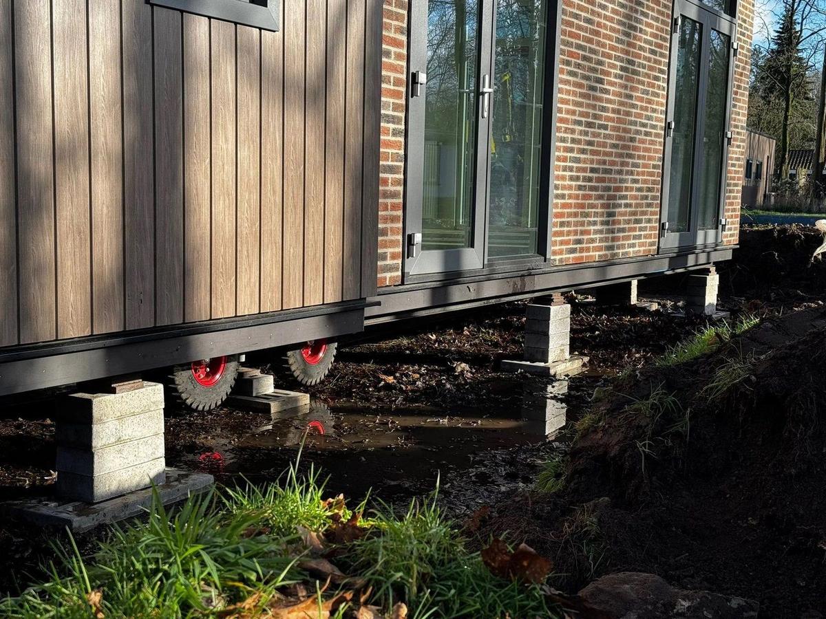 Woning met bakstenen gevel op bielzen, met een kraan op de achtergrond