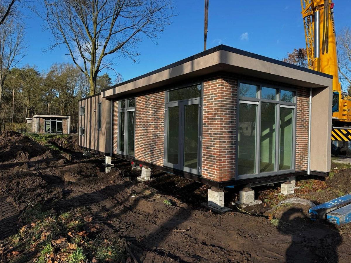Een woning met bakstenen gevel en grote ramen op bielzen